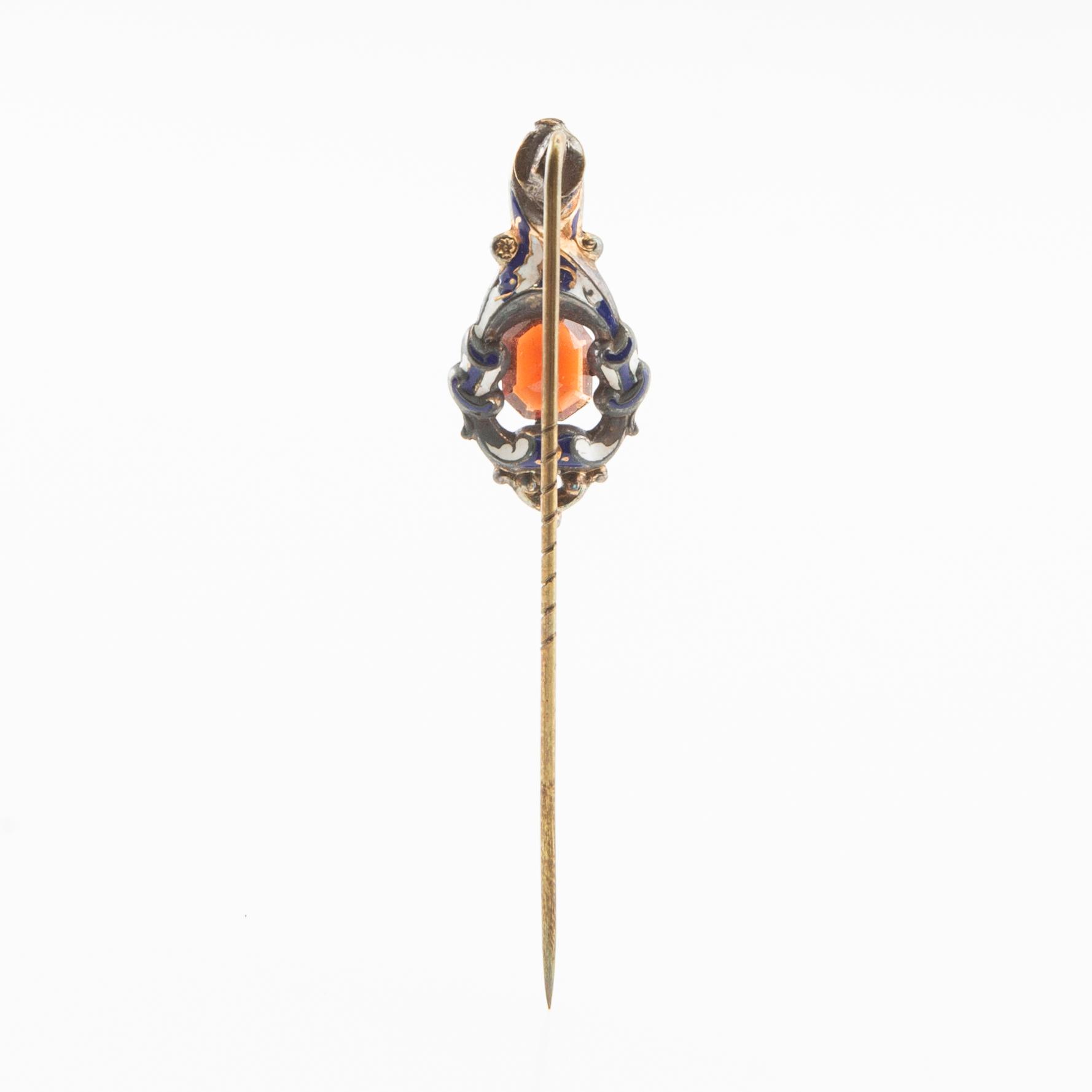 Kravattnål av förgylld mässing med dekor av emalj och en fasetterad granat, 1800-talets andra hälft.